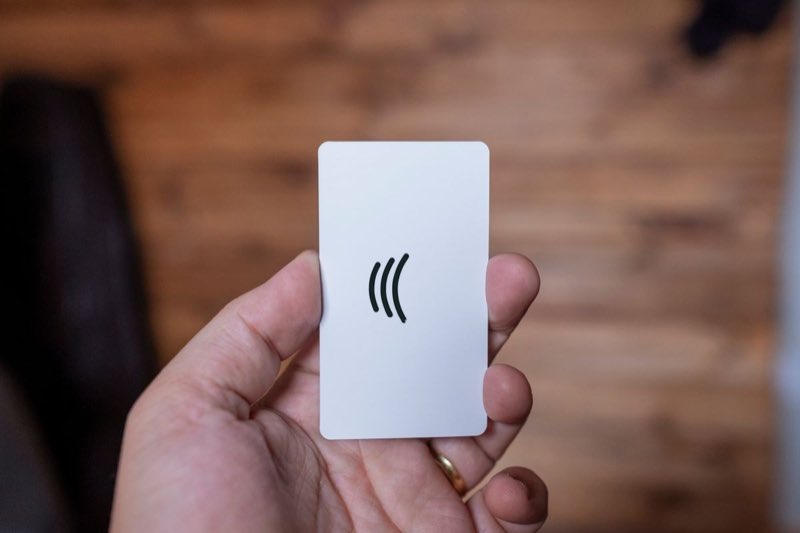 Una mano sostiene una tarjeta blanca con el símbolo de las ondas del NFC impreso.